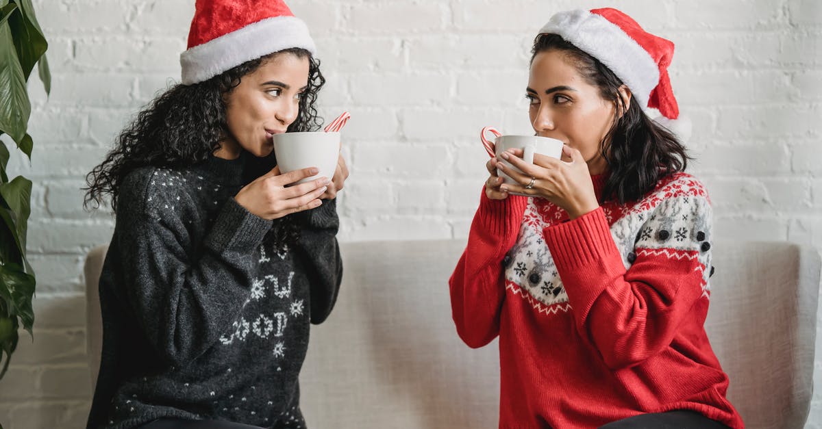 Separating chocolate-coated cookies stuck together - Multiracial girlfriends sitting on sofa at home and drinking cocoa