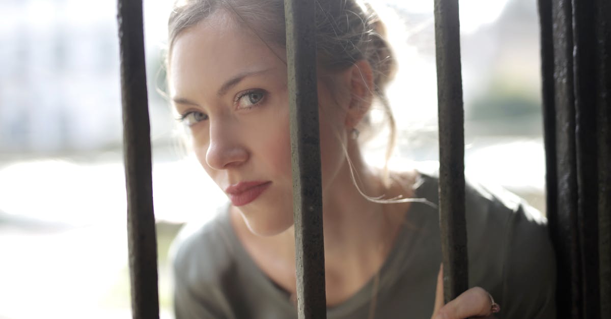 Serious buildup outside of cast iron skillet - Young beautiful female with bewitching look leaning on iron black bars and looking at camera while standing at fence on sunny day