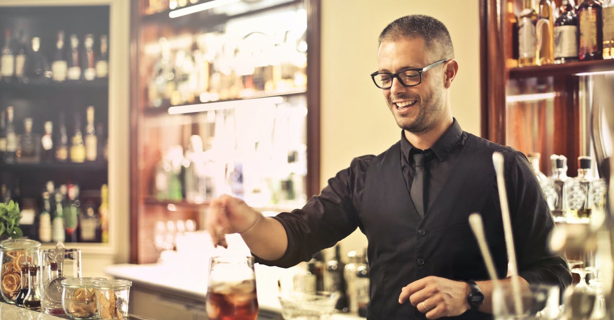 Shaking cocktails without bar equipment - Happy young male barkeeper standing at counter and preparing alcohol cocktail for order while working in modern pub