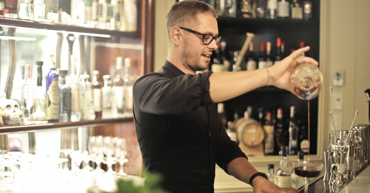 Should boiled legumes cool before processing? - Side view of positive young barman in black uniform and eyeglasses pouring wine into glass while working at bar counter in modern restaurant