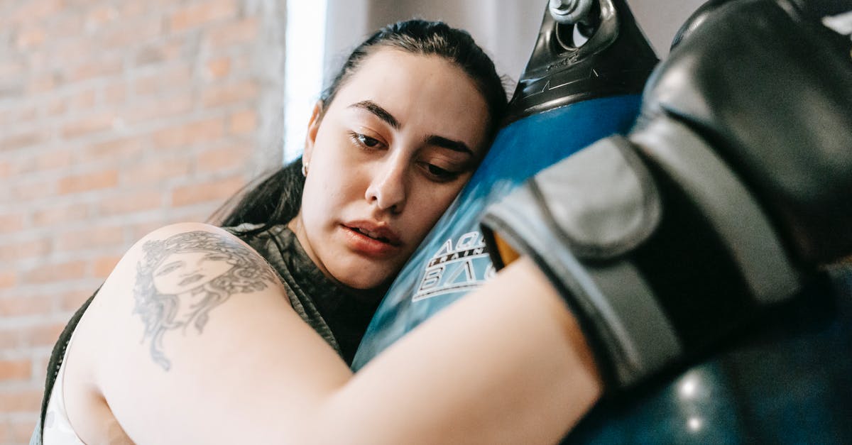 Should I bag hard candy or not? - Low angle side view of exhausted young female in boxing gloves having pause in hard training in fitness center