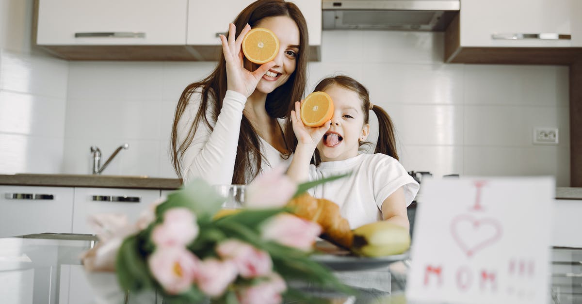 Should I eat nipples? - From below of cheerful mother and daughter in domestic clothes smiling and playing with oranges while sitting together at table with bouquet of tulip and drawing of child