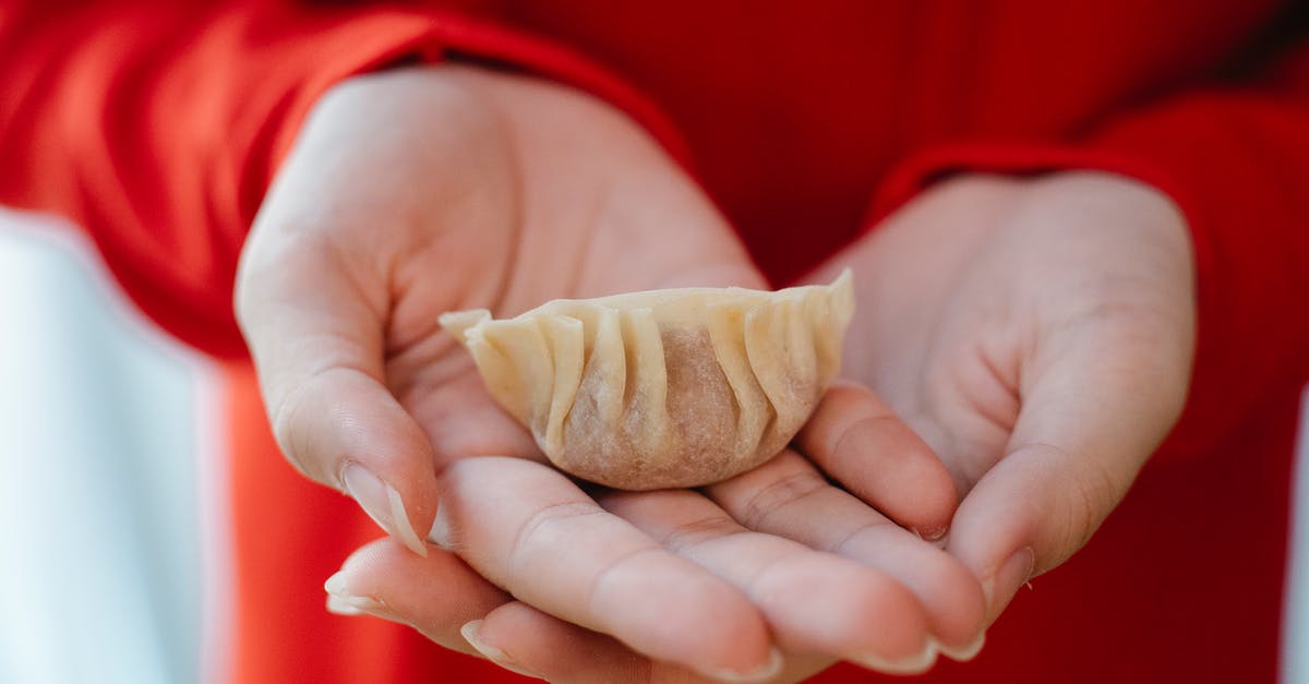 Should I freeze gyoza before or after cooking? - Crop unrecognizable person in red clothes showing homemade jiaozi dumpling in hands in daylight
