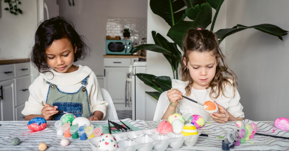 Should I refrigerate eggs? - Concentrated multiracial girls painting white eggs with paintbrushes while sitting at table with paints in kitchen during Easter holiday at home