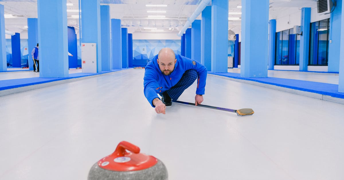 Should I throw moldy Strawberries away? - Concentrated sportsman with beard in blue uniform squatting down and looking at sliding stone with red handle during curling game on modern ice rink