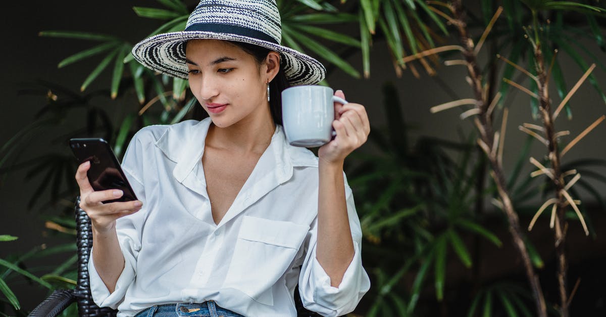 Should I use dried or fresh chilli/ginger in chai tea? - Young Asian lady wearing stylish outfit sitting in wicker armchair in greenery and browsing smartphone while drinking hot beverage