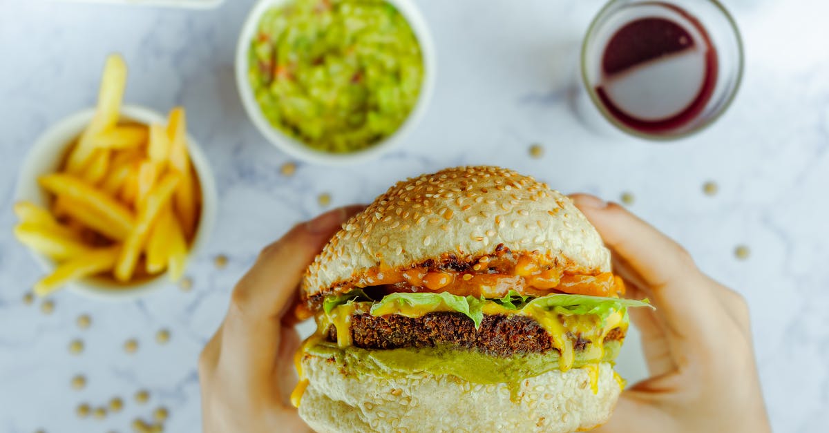 Should Pickle Slices be Above or Below the Hamburger - From above of faceless person eating big hamburger with cutlet between melted cheese and lettuce at table with fast food on blurred background