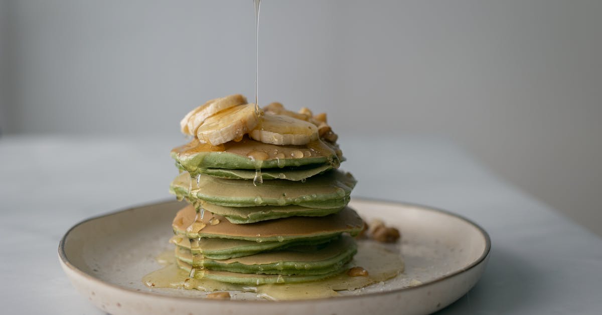 Should syrup or pastry be cooled when pouring on to Baklava? - Unrecognizable person pouring honey on stack of appetizing green pancakes topped with bananas and walnuts and served on plate on table