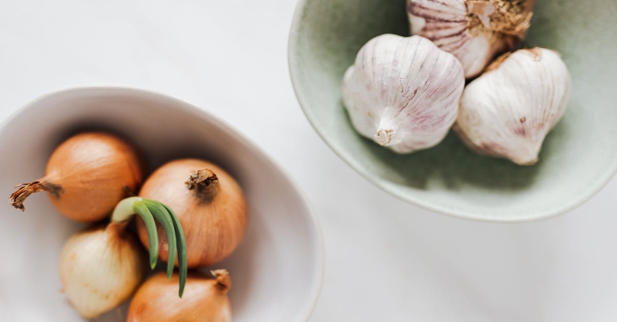 Slimy inside of green onions [duplicate] - Top view of ceramic bowls of garlic bulbs and onions with green sprouts on white marble table