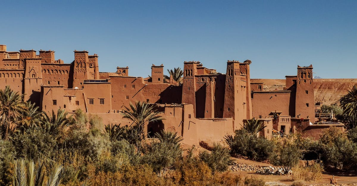 Smen - Moroccan fermented butter.. best clarified or not? - Exterior of old masonry buildings with square shaped windows near dry sandy terrain with growing palm trees and grass under blue sky