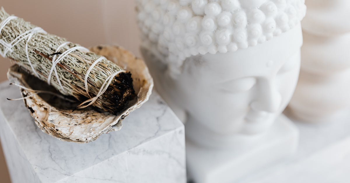 Smoke coming from oven - From above of sage candle in bowl placed on white marble shelf near plaster Buddha bust and creative shape vase for home decoration