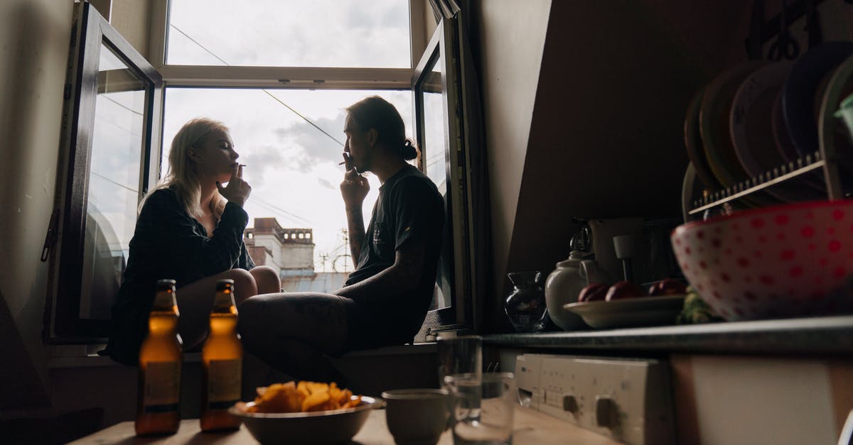 Smoking without wood chips - A Man and a Woman Sitting Face to Face on a Windowsill while Smoking Cigarette