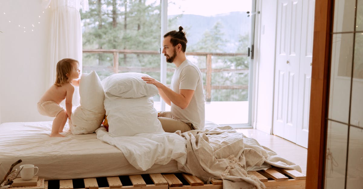 Solid honey in dragon's beard candy? - Side view of serious bearded father in casual clothes playing with little child with pillows on comfortable bed in light bedroom at home