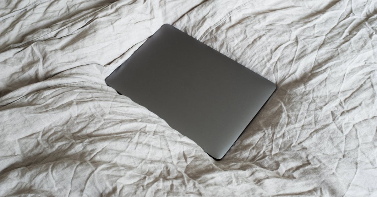 Something dark gray coming off of sheet pan after scouring - From above of closed dark gray portable computer located on large soft and crumpled cotton bed sheet in apartment in light room