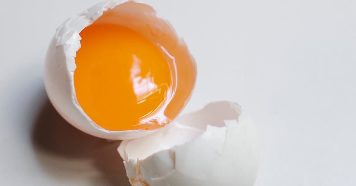 Sous vide egg white falling apart on cracking - Top view of broken raw egg with yellow yolk and white eggshell on white background in light kitchen during cooking process