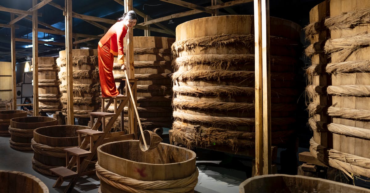 Soy Sauce storage container - Full body of Asian female worker with instrument standing near row of barrels in fish sauce factory