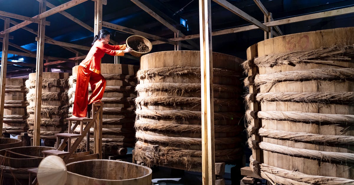 Soy Sauce storage container - Full body of female adding ingredient from bowl into wooden barrel with fish sauce in factory