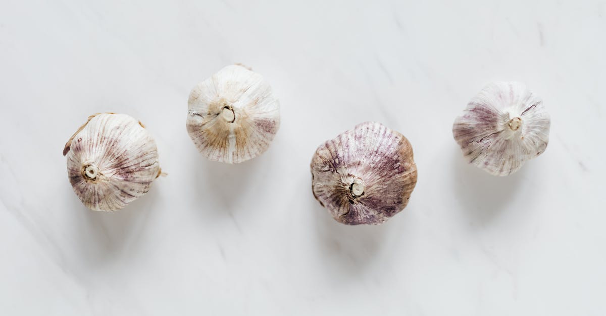 Spicy soy, seed bitterness and placental capsaicin - Top view of raw whole unpeeled aromatic garlic placed next to each other on white marble surface before cooking process