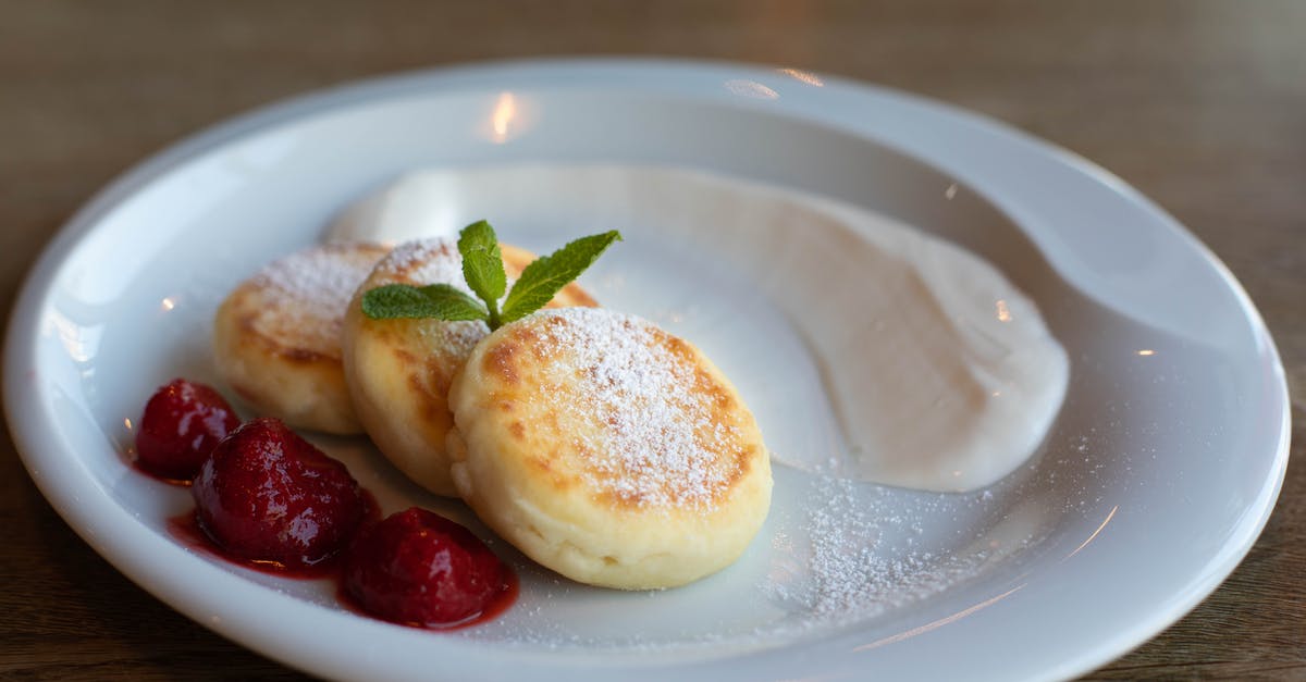 Storing Cream Cheese Icing - Top view of round plate with golden curd fritters decorated with powdered sugar and fresh mint near strawberry jam with whole berries and sour cream