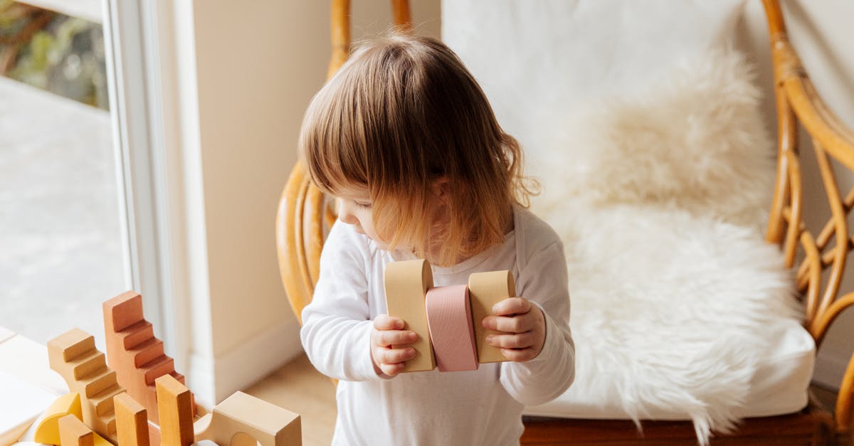 Storing knives: wood block or magnetic stripe? - From above of cute little child in white wear holding wood blocks for building while standing near wicker armchair