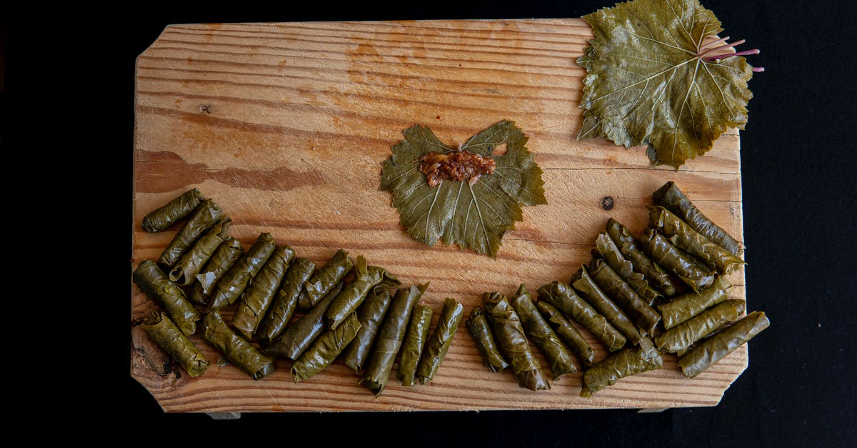 Subsitute in this kale and grape recipe - Top view of sarma rolls near vine leaves with meat filling on wooden table on black background