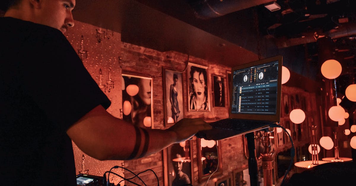 Substitute for a Standing Mixer using a paddle - Male DJ in black tee shirt standing behind equipment and selecting songs on laptop during party in bar