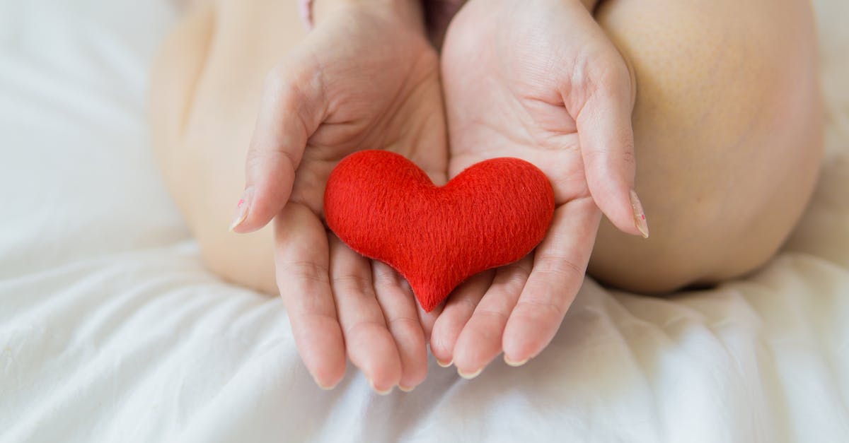 Substitute for blood? - Unrecognizable female sitting with bare legs on white sheet with small red heart in hands in light room in daytime