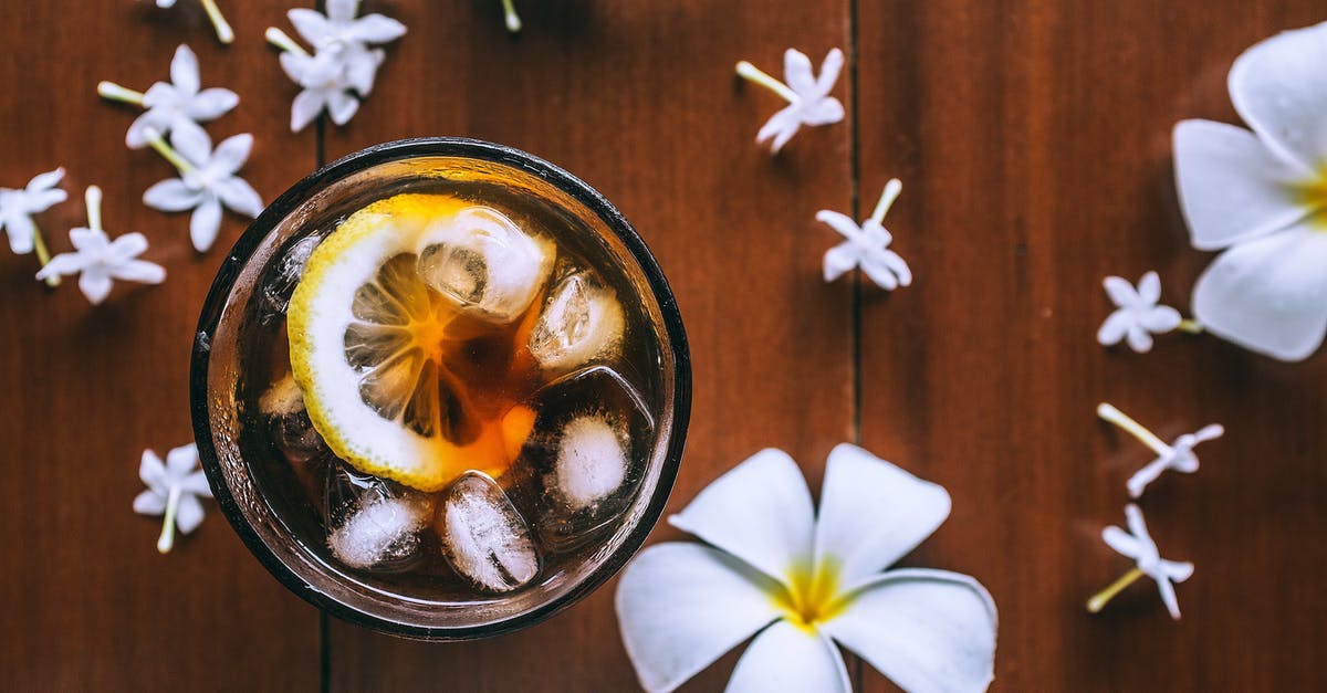 Substitute for fresh lemons - I need to make 70 liters of homemade lemonade - Top view of glass with fresh drink with slice of lemon and ice cubes on wooden background with plumeria flowers