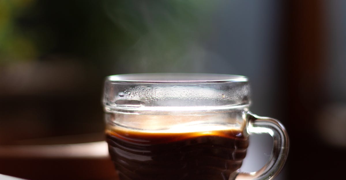 Substitute instant coffee for brewed black coffee - Delicious aromatic black coffee with steam in creative design glass cup with shiny surface on table for breakfast on blurred background