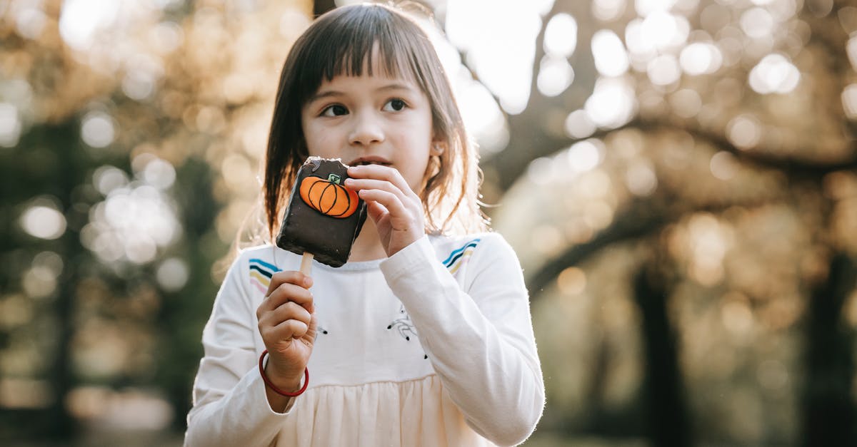 Substituting white chocolate in Julia Child's mousse - Adorable little girl in white clothes standing in park with bitten tasty chocolate Halloween sweet on stick and looking away