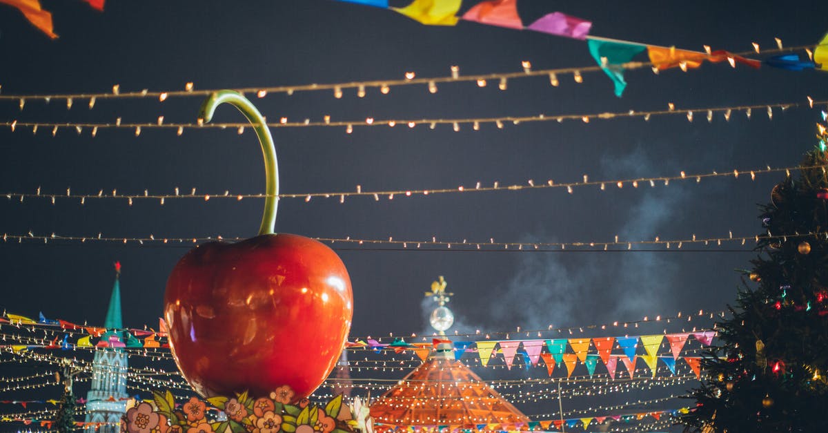 Substitution for idealmjöl - Big red glossy toy apple on roof of building on fairground against dark sky in evening city park decorated to winter holidays