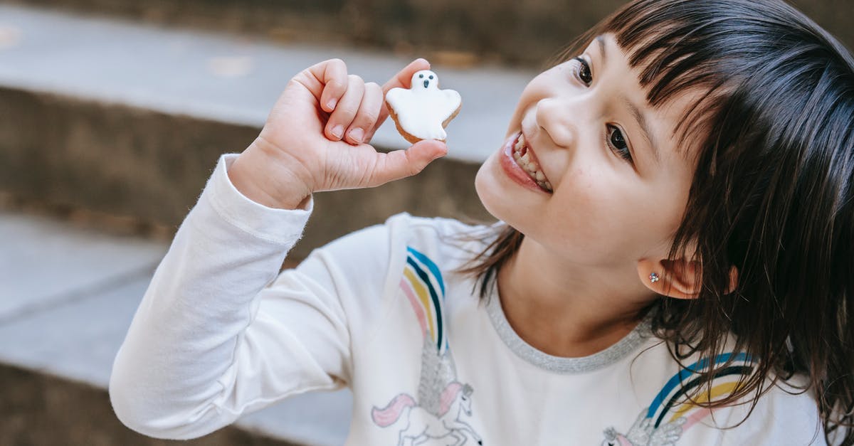 Sugar content of food - Adorable smiling girl with cookie made for Halloween holiday sitting on stone stairs