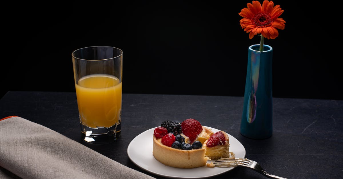 Sugar syrup with orange juice foams excessively - High angle of plate with delicious cheesecake decorated with berries placed on table with orange juice and vase with red gerbera