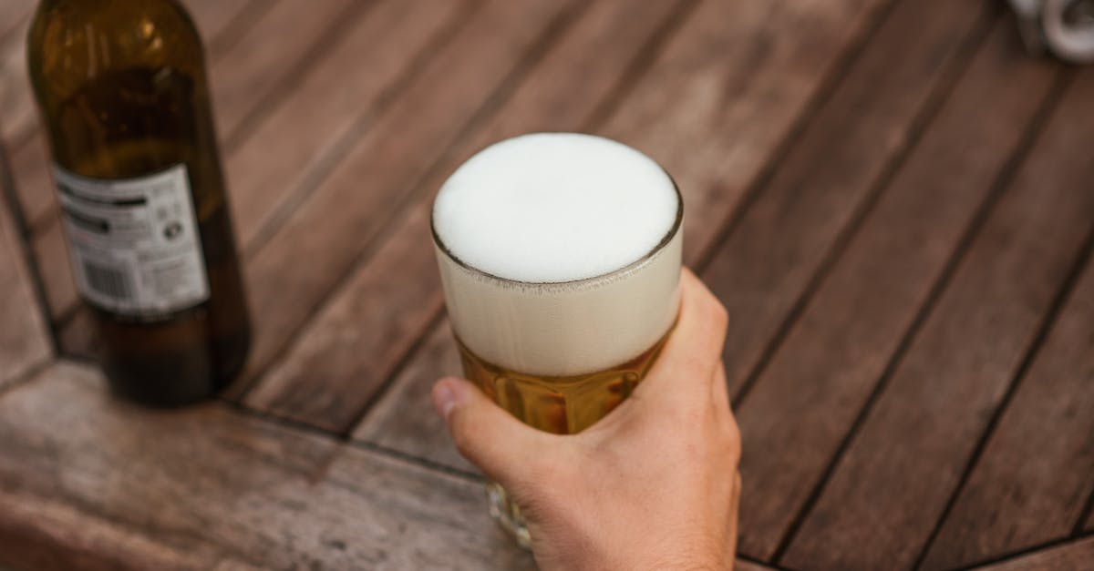 Taste difference of bottled beer vs. canned beer - From above of crop anonymous male with glass mug of cold beer with foam resting at weekend