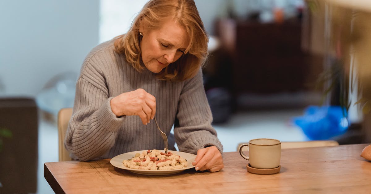 Tea taste changes if watered down after steeping - Emotionless senior female wearing blue sweater enjoying yummy vegetable pasta while sitting at table in living room