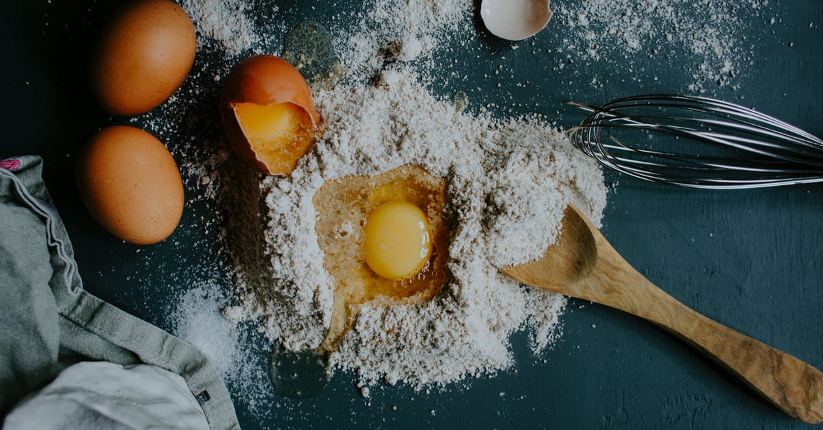 Techniques for mixing bread dough with stand mixer - Top view pile of flour on table with broken egg arranged with wooden spoon and metal corolla during preparation of homemade dough