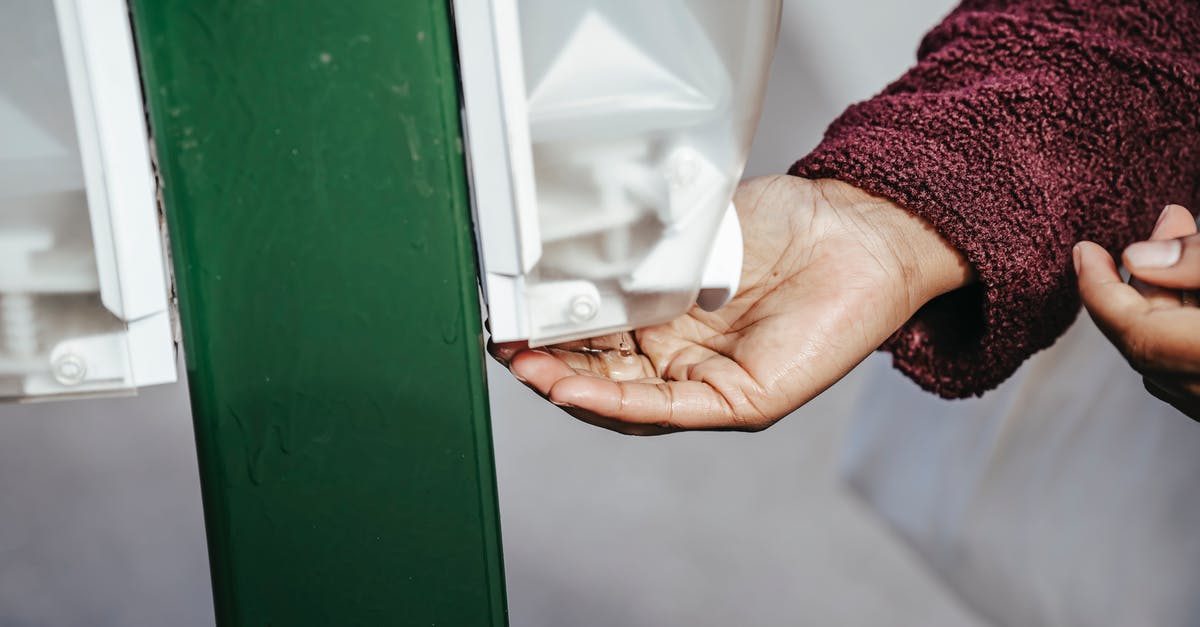 Teflon-coated pans: are they ever dishwasher-safe? - Crop anonymous black female in warm coat standing in street and using sanitizer in daylight