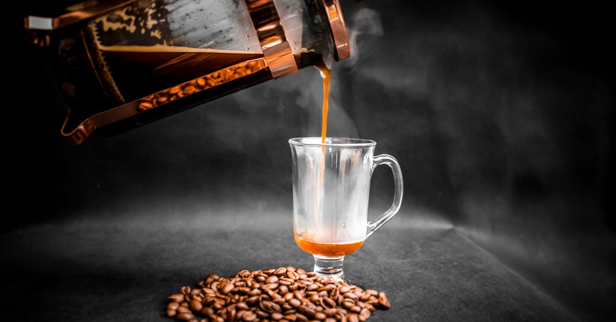 The best way to clean a French Press coffee maker - Aromatic hot coffee being poured from French press into elegant glass with pile of coffee beans beside on black background