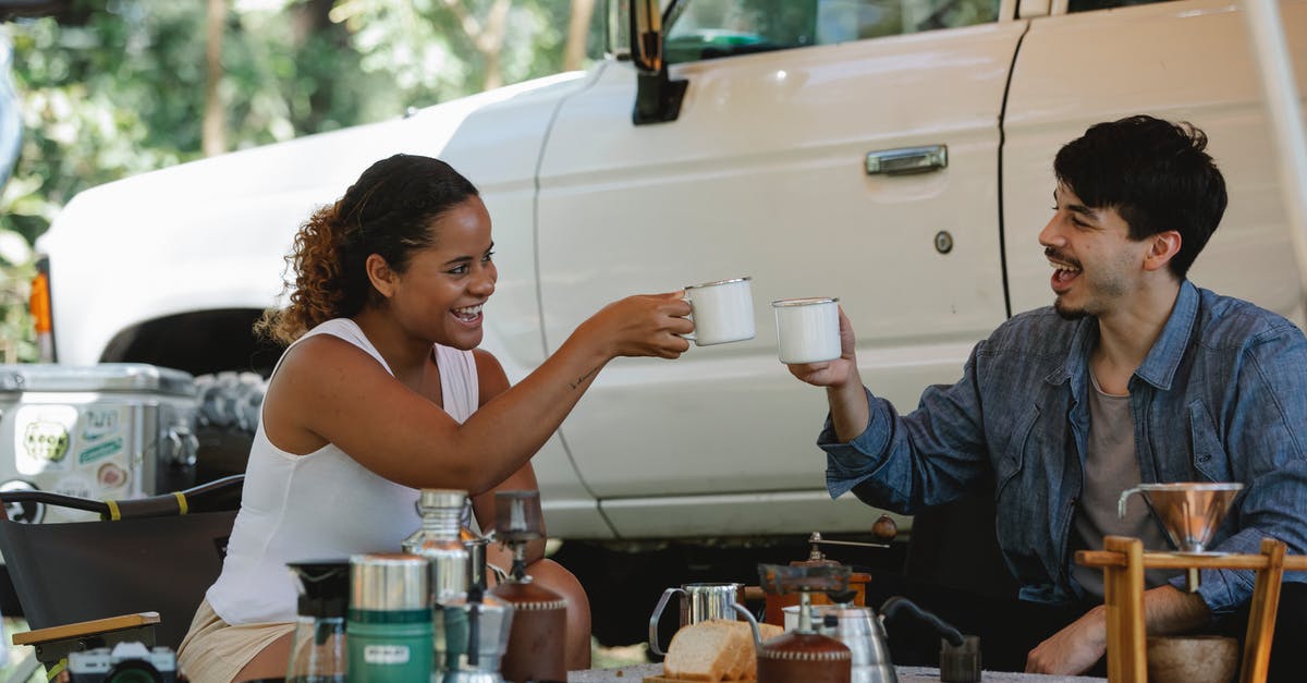 the whistle on the kettle keeps popping off - Joyful young diverse couple clinking coffee cups during picnic in nature