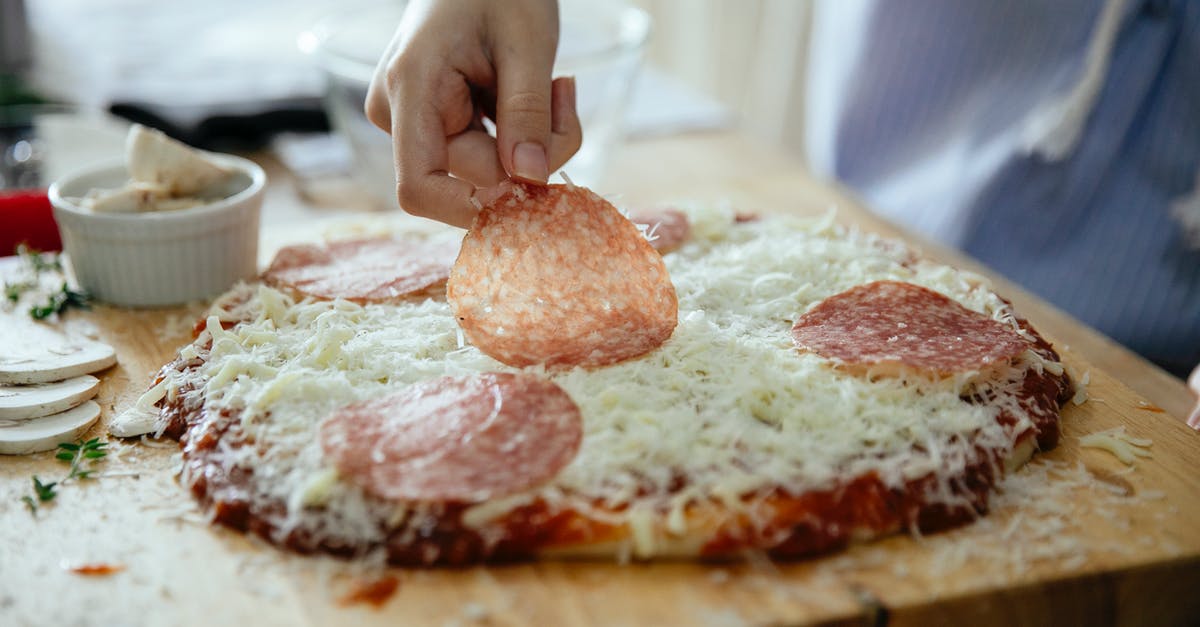 Thicker gelatin layer at the bottom of the dish - Crop anonymous person putting slice of salami on yummy homemade on wooden cutting board while cooking in kitchen