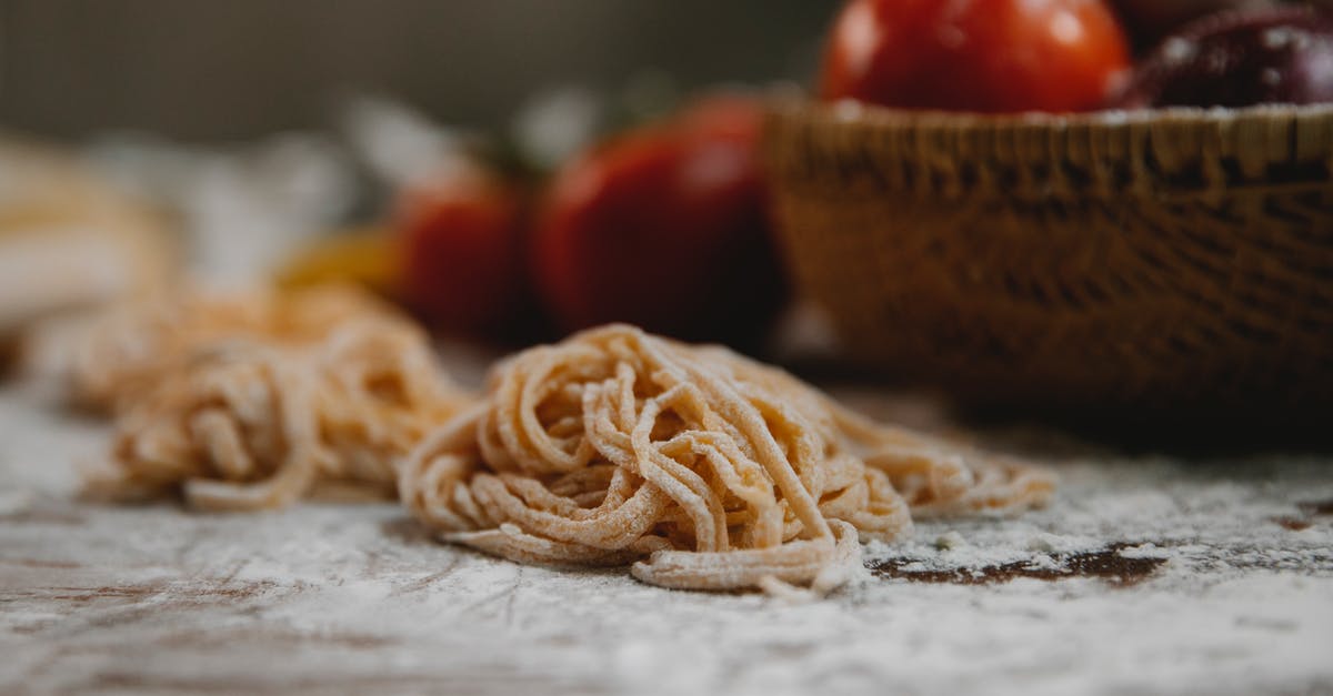Thinning Tomato paste - Thin spaghetti arranged with timber bowl with tomato and vegetables on table covered with flour