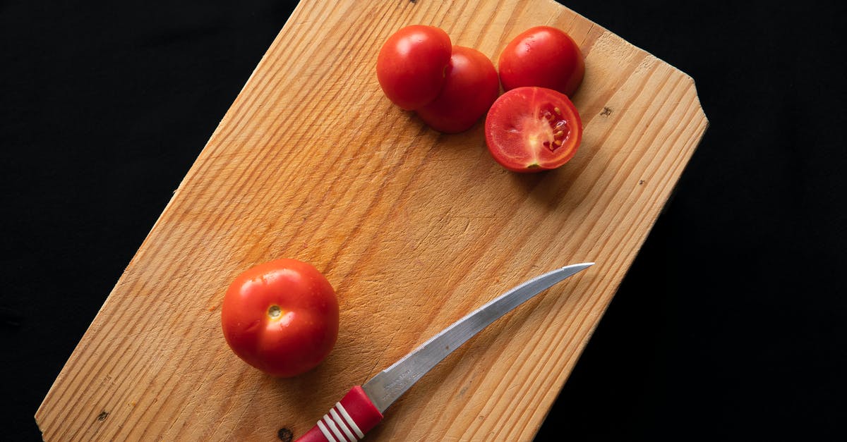 Thinning Tomato paste - Top view of thin sharp knife placed near red fresh tomatoes on timber board on black background