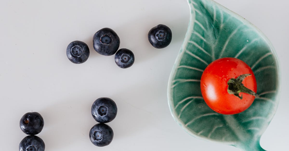 Tomato sauce - tomatoes, then juice vs tomatoes & juice - Minimalistic composition of fresh tomato on small designer platter near blueberries on gray background