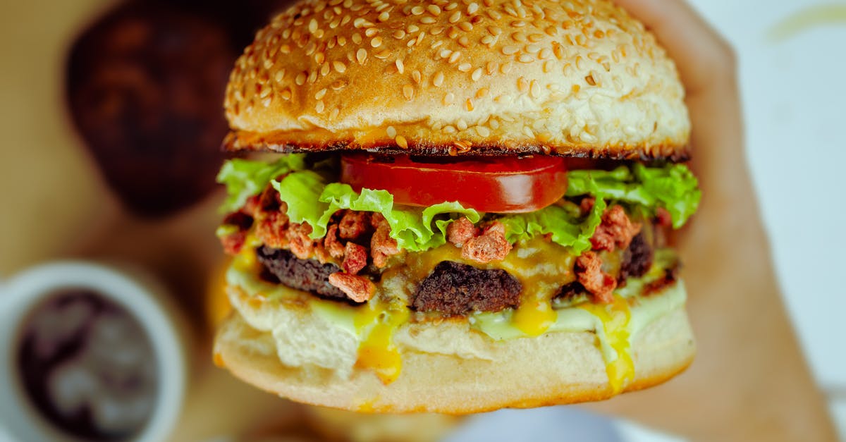 Tomato Sauce Turns Dark/Sweet - Unrecognizable person eating big delicious hamburger with dark brown cutlet and fresh vegetable between buns covered with edible seeds