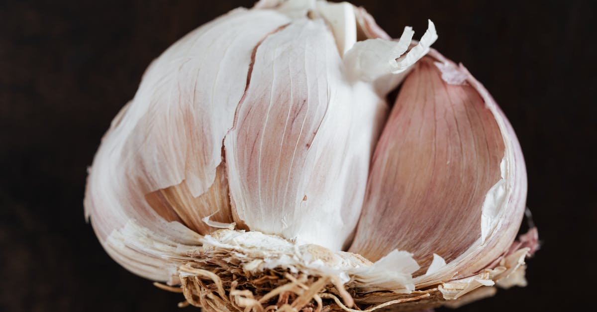 Tools to peel and crush a whole garlic bulb - Top view of fresh halved garlic in peel placed on dark brown surface before training in restaurant