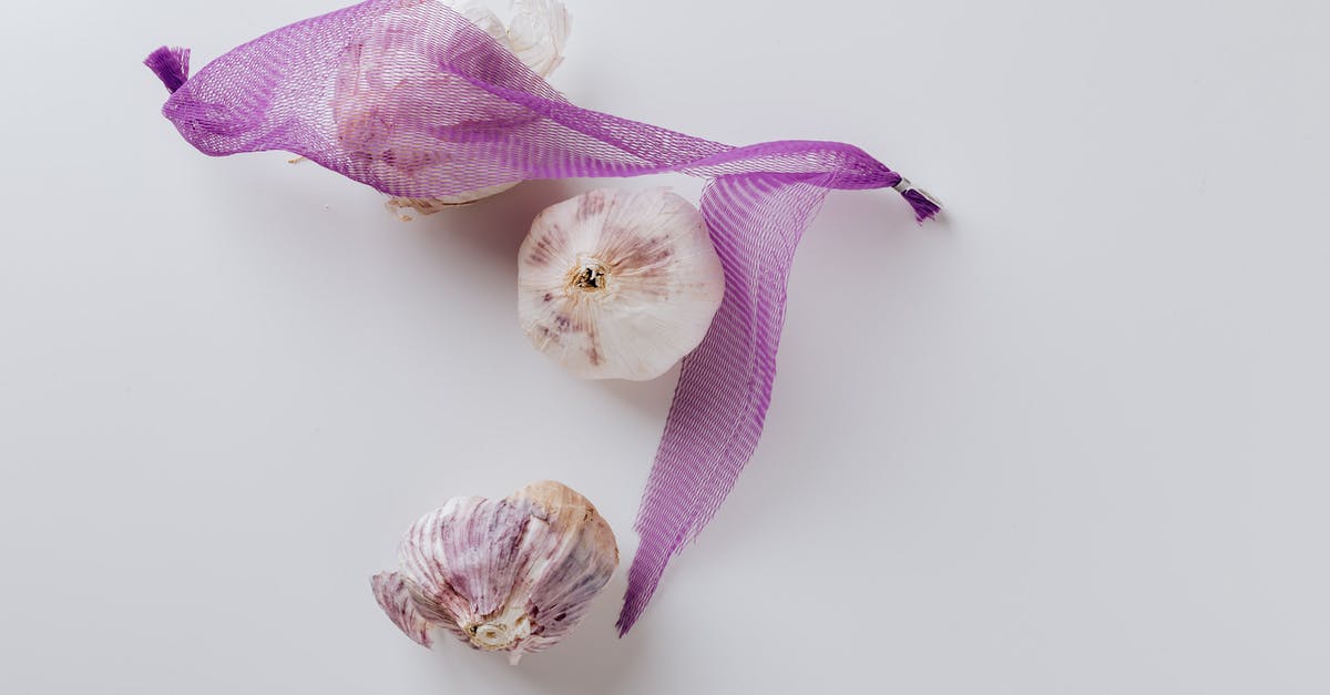 Tools to peel and crush a whole garlic bulb - Composition of garlic bulbs with purple net on white background