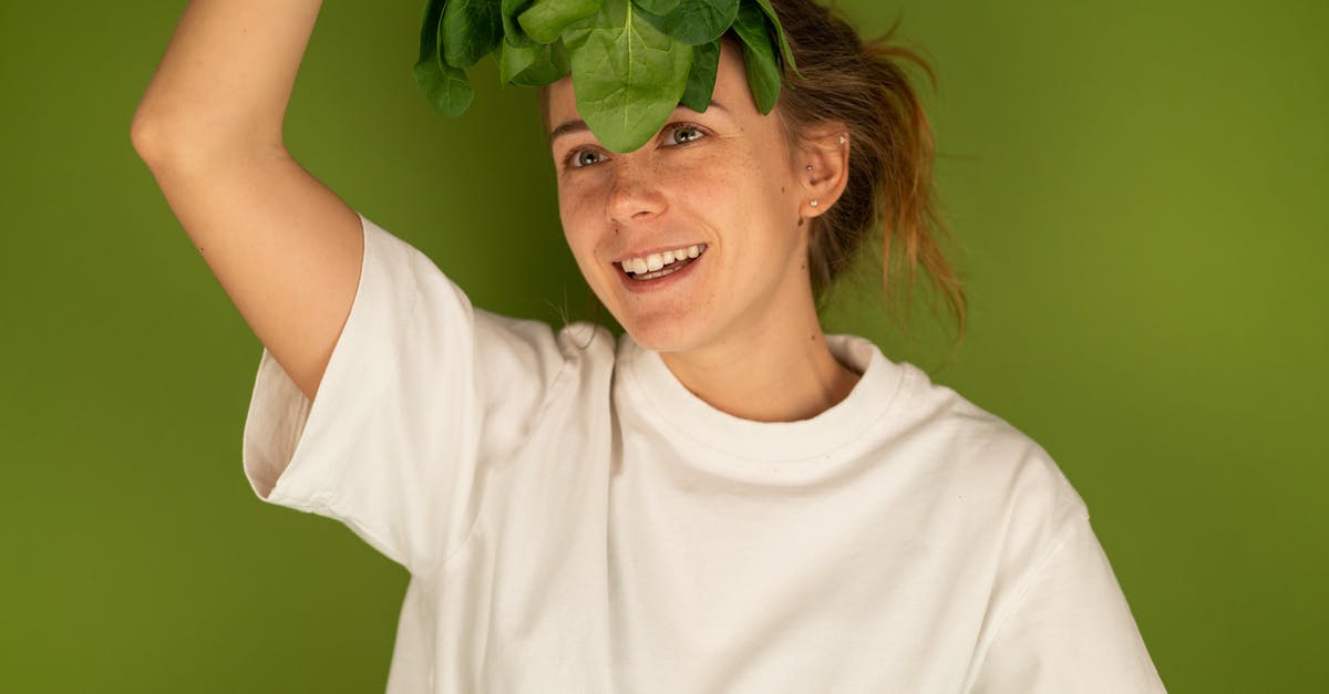 Trying to improve a vegetarian wrap by adding spinach - Smiling woman with spinach leaves on green background