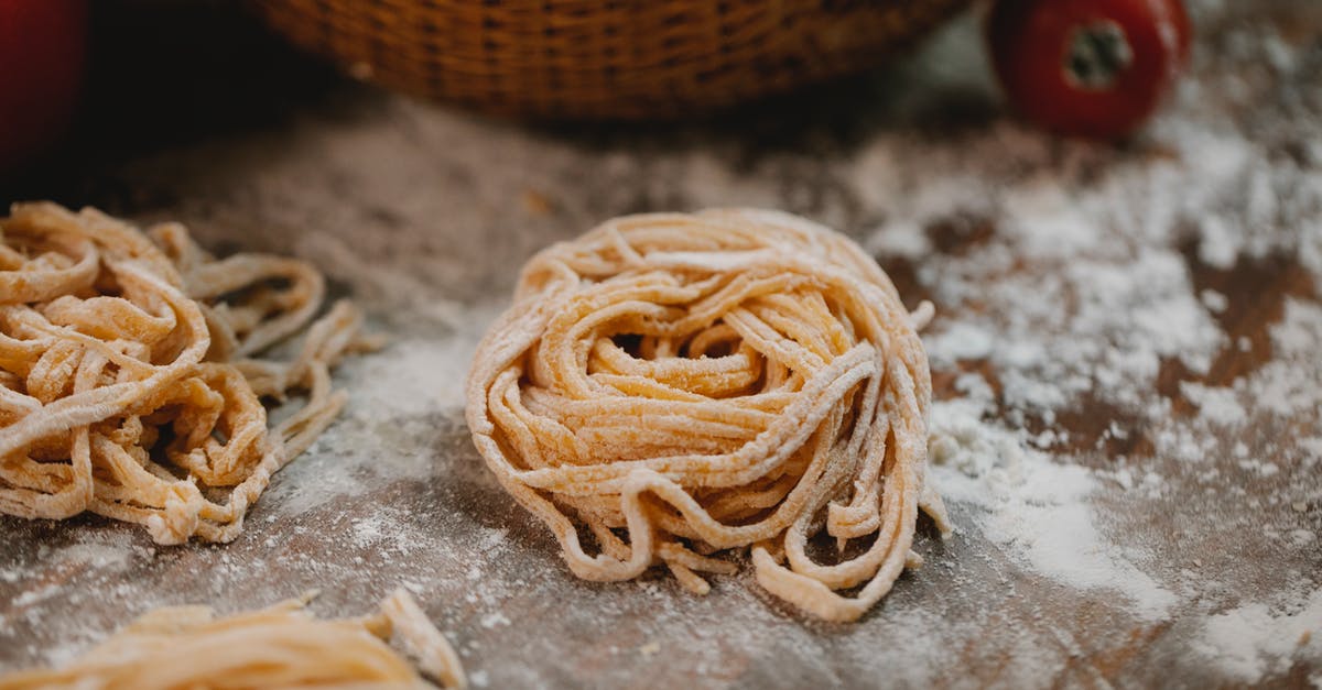 Underside of dough in proofing basket pulls apart - From above nests of fresh homemade uncooked spaghetti placed on wooden table with scattered flour in kitchen