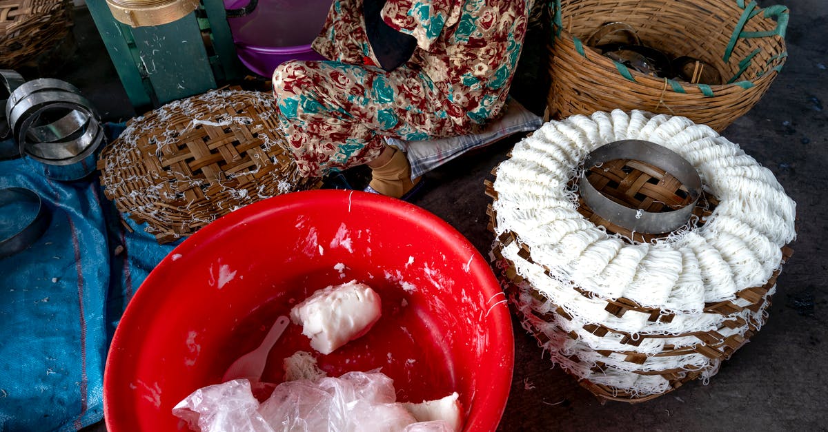 Underside of dough in proofing basket pulls apart - From above of tool for production of traditional Vietnamese noodles with white dough near plastic container and wicker basket