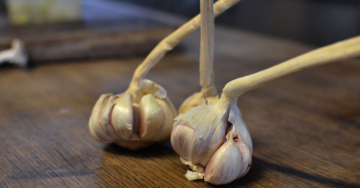 Unpeeled garlic cloves in French / Belgian cooking? - High angle of fresh unpeeled garlic bulbs placed on wooden table in kitchen